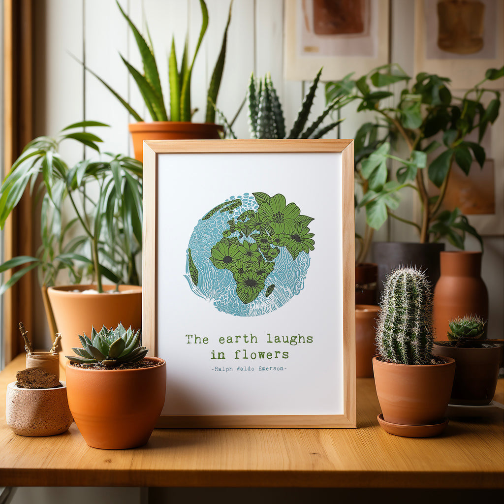 Floral earth screen print in a wood frame sitting on a table surrounded by potted plants and cacti