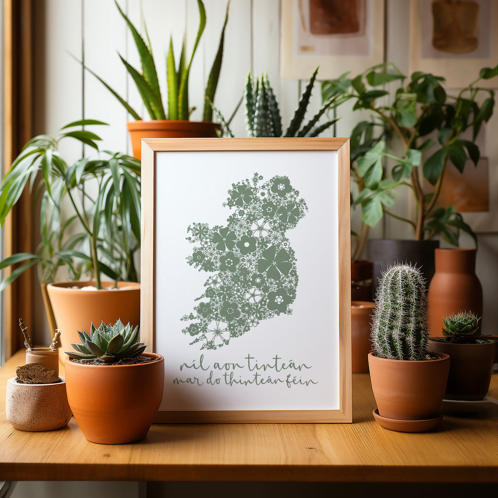 Green Irish Ireland screen print in a wood frame sitting on a table surrounded by potted plants and cacti