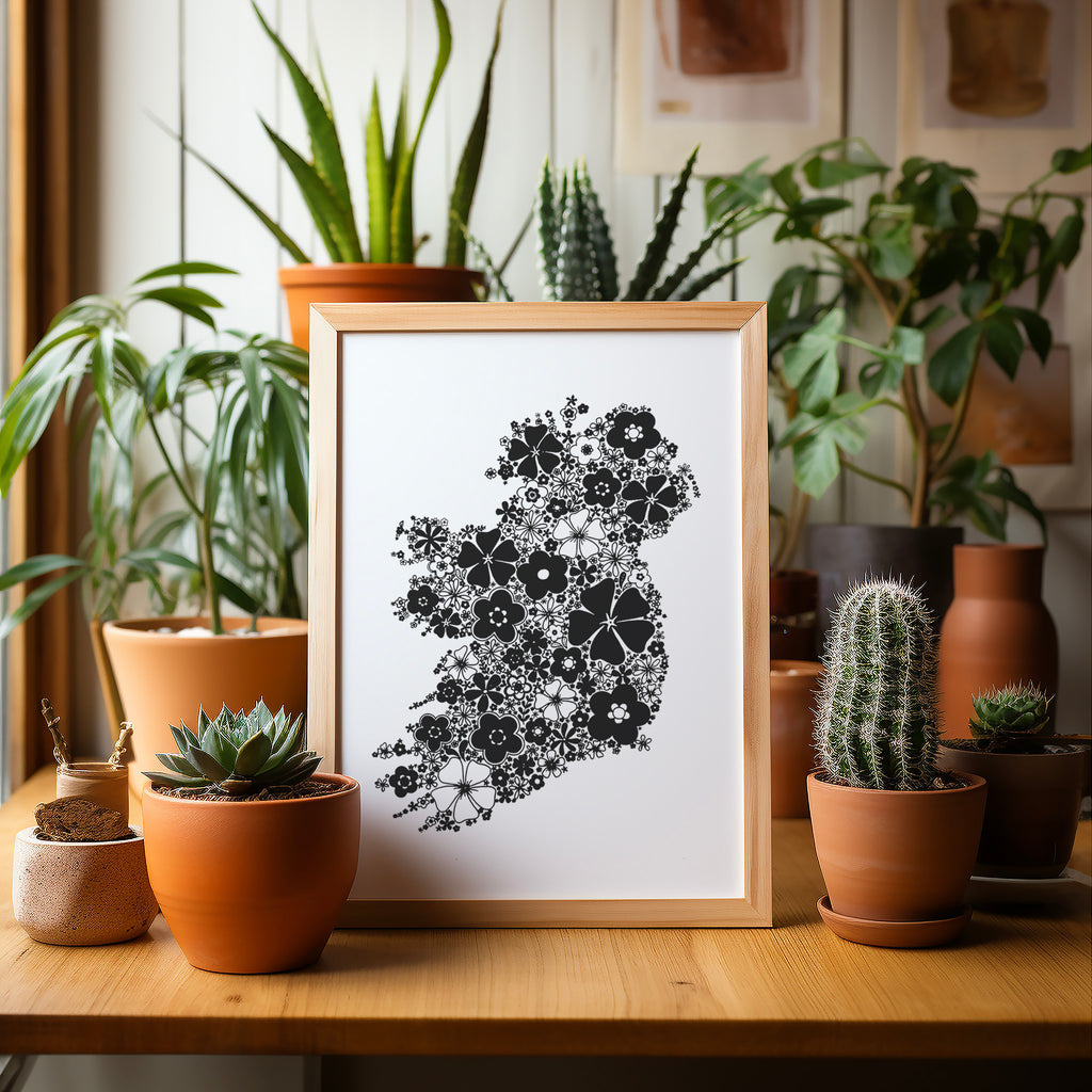 Black floral Ireland screen print in a wood frame on a table surrounded by potted plants and cacti