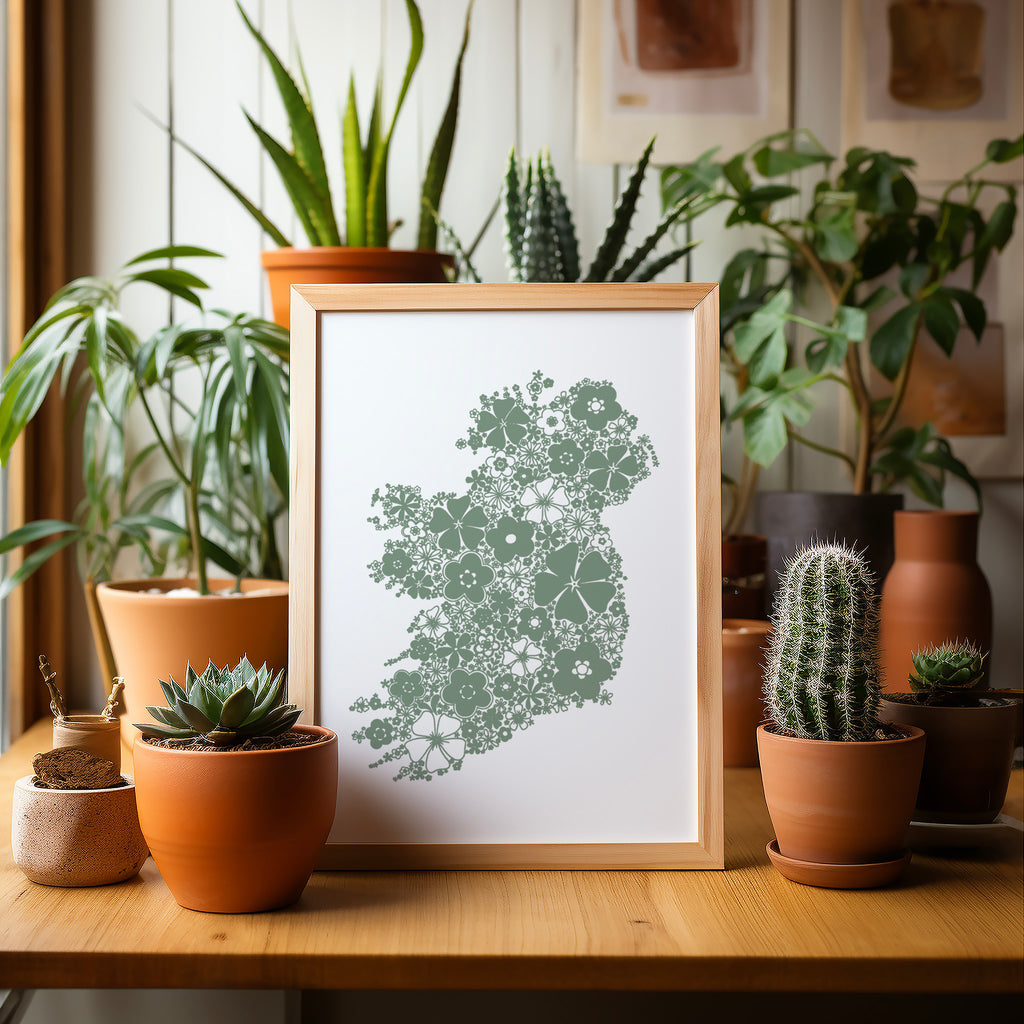 Green floral Ireland screen print in a wood frame on a table surrounded by potted plants and cacti