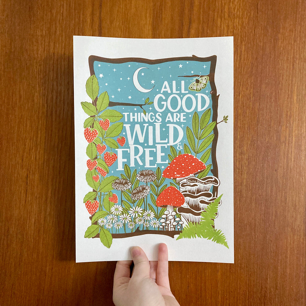 Holding up our screen print with our 'All good things are wild and free' design hand printed in brown, blue, green and red.  Print held up in front of wood.