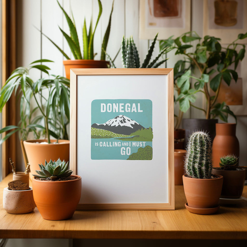 Our 'Donegal' screen print, in an A4 frame sitting on a table, surrounded by potted cacti and plants.