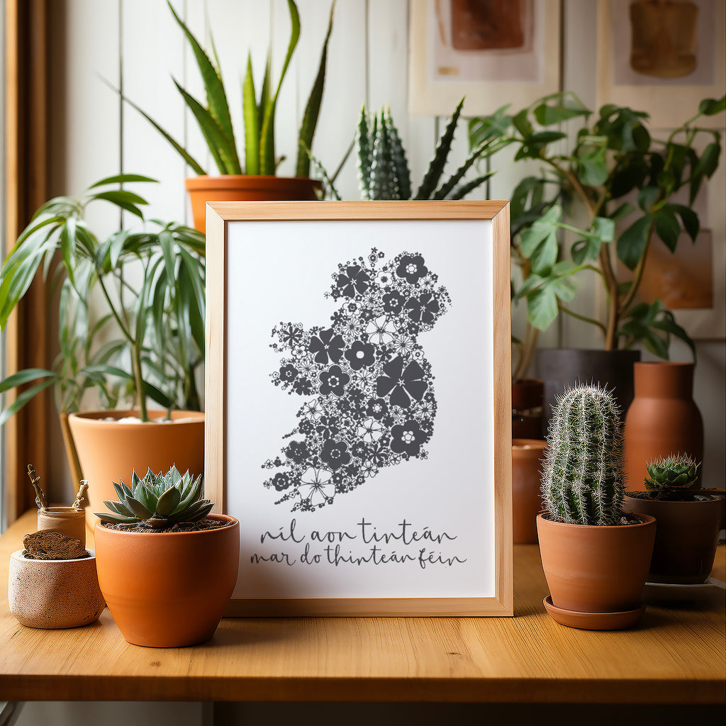 Grey Irish screen print with Ireland in a wood frame sitting on a table surrounded by potted plants and cacti