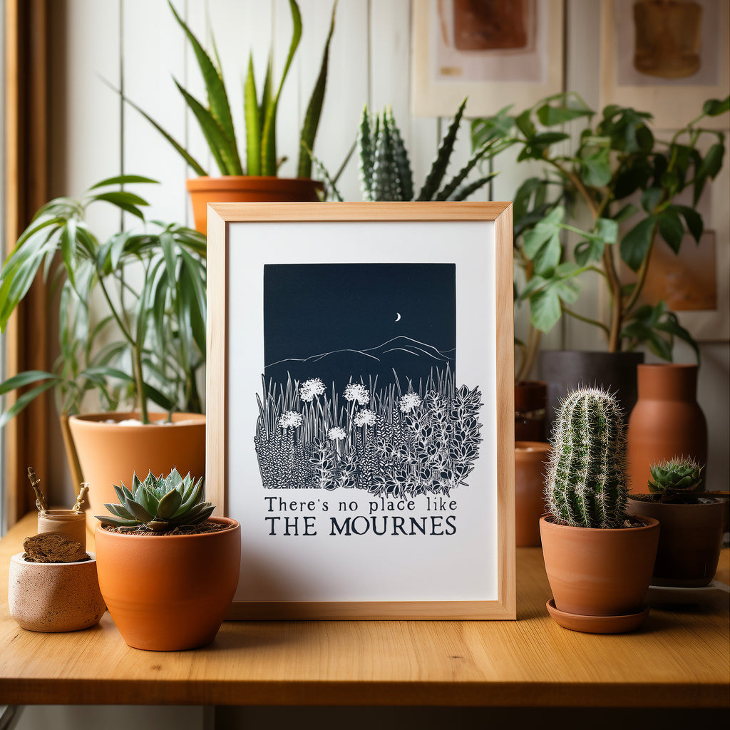 Midnight blue Mournes screen print in a wood frame on a table surrounded by potted plants and cacti