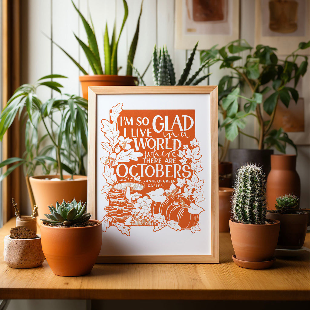 Our 'I'm so glad I live in a world where there are Octobers' screen print framed and sitting on a table with many potted cactus and plants