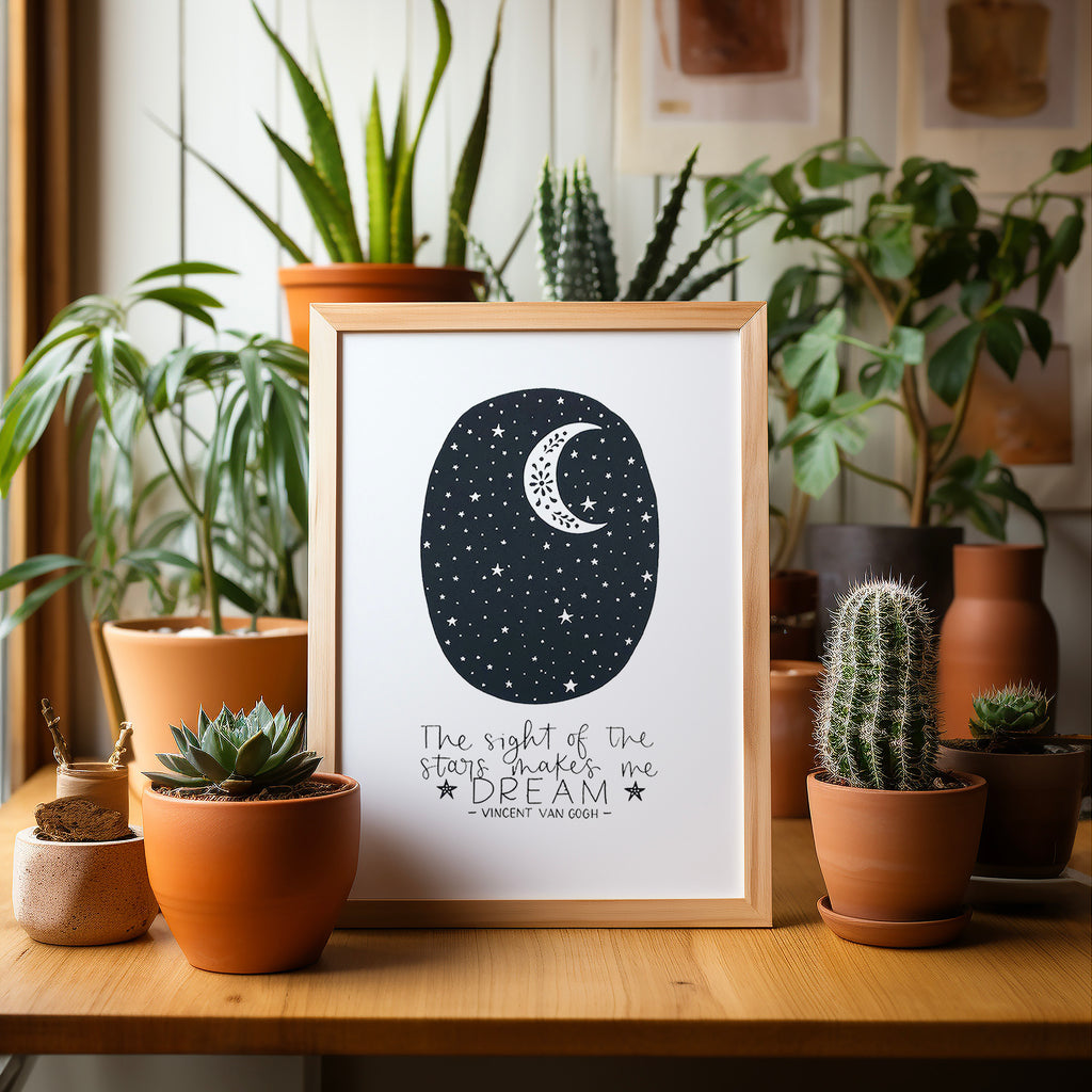 Stars screen print in a wood frame on a wood table surrounded by potted plants and cacti