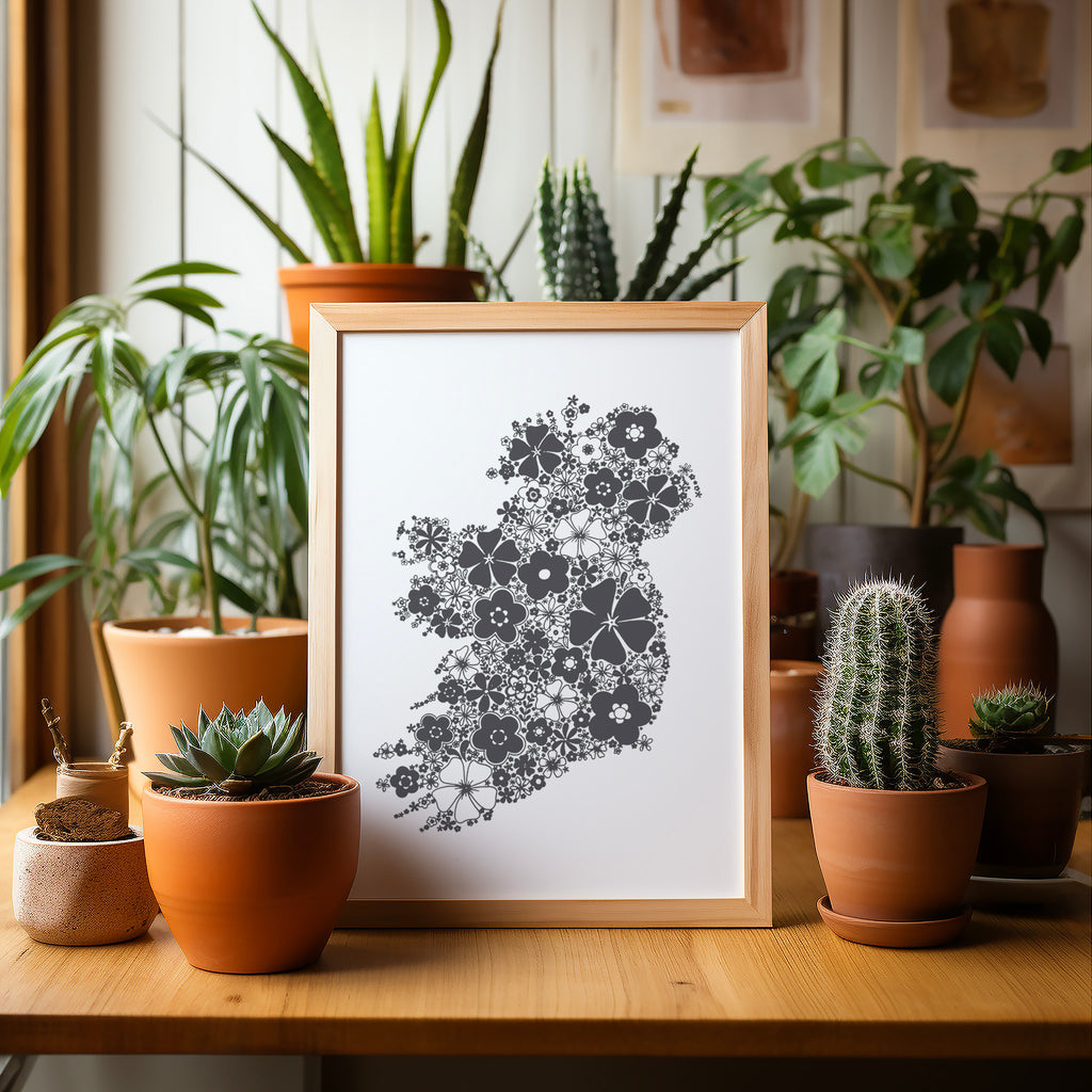 Grey floral Ireland screen print in a wood frame on a table surrounded by potted plants and cacti