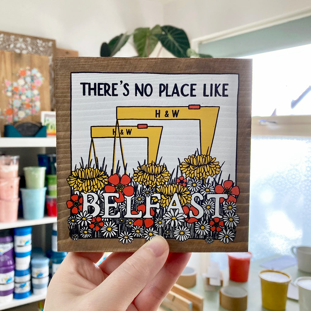 Belfast wood sign held up in studio with different colours of paints sitting in the background.