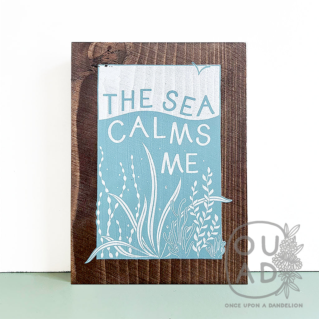 The sea calms me, wood sign sitting on a light green shelf against a white wall